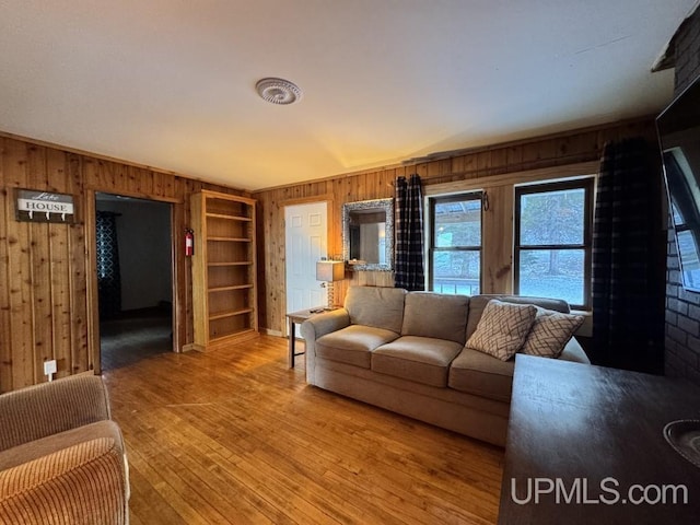 living room with built in shelves, hardwood / wood-style flooring, and wooden walls