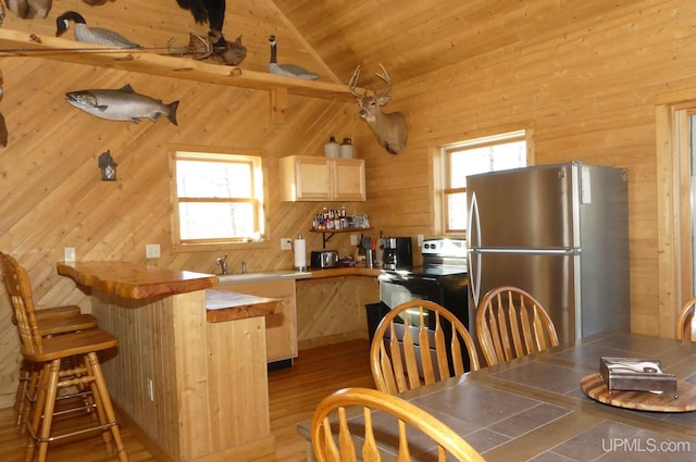 kitchen with lofted ceiling, stove, light brown cabinetry, and stainless steel refrigerator