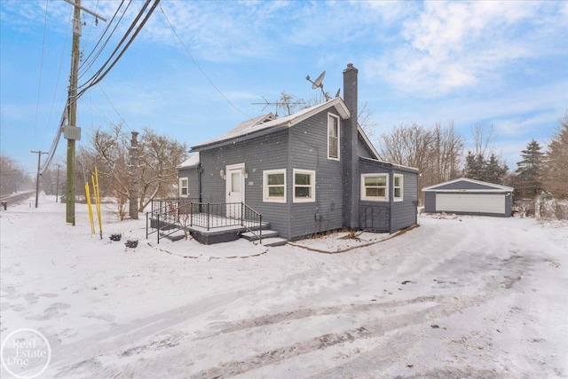 snow covered back of property with a garage and an outdoor structure