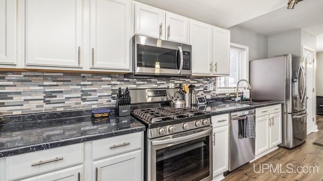 kitchen with dark wood-type flooring, dark stone counters, white cabinets, sink, and appliances with stainless steel finishes