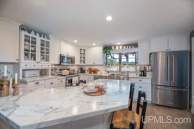 kitchen with white cabinetry, light stone countertops, sink, a breakfast bar, and appliances with stainless steel finishes