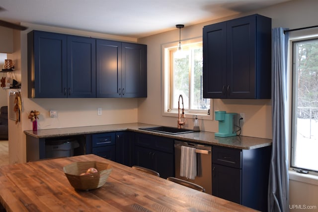 kitchen featuring wood counters, sink, stainless steel dishwasher, blue cabinetry, and decorative light fixtures