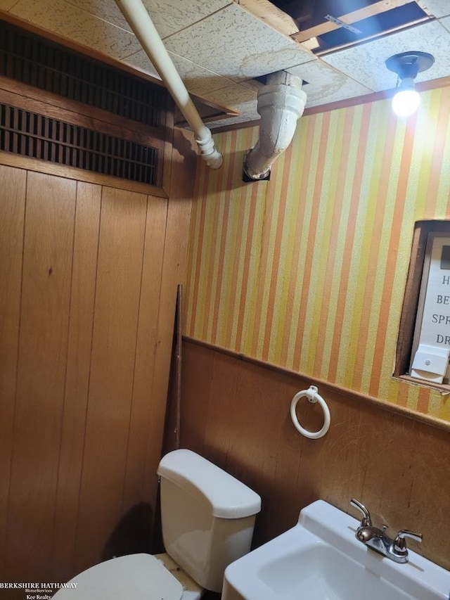 bathroom with sink, toilet, and wood walls