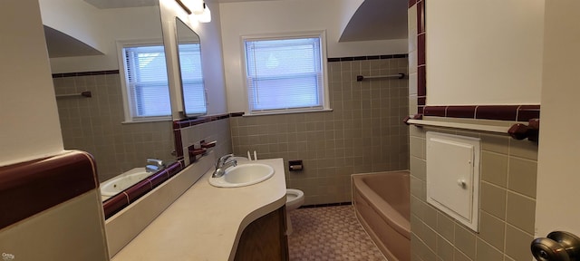 bathroom with a washtub, vanity, tile walls, and toilet