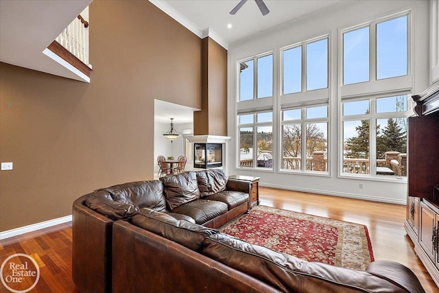 living room with a high ceiling, light hardwood / wood-style flooring, ceiling fan, and crown molding