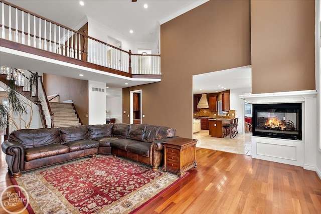 living room featuring a multi sided fireplace, light hardwood / wood-style flooring, a towering ceiling, and ornamental molding