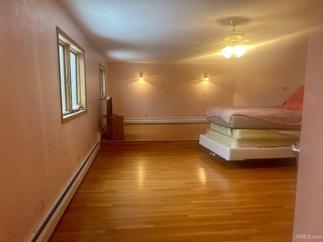 unfurnished bedroom with ceiling fan, hardwood / wood-style flooring, and a baseboard heating unit