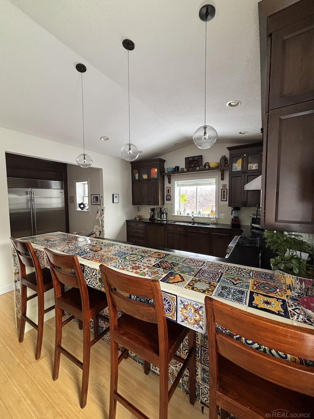 kitchen featuring dark brown cabinetry, hanging light fixtures, stainless steel built in refrigerator, light hardwood / wood-style floors, and lofted ceiling