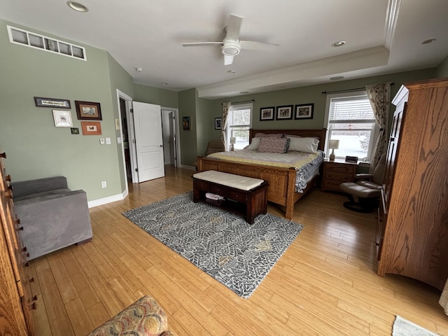 bedroom with light hardwood / wood-style floors, a raised ceiling, ceiling fan, and crown molding