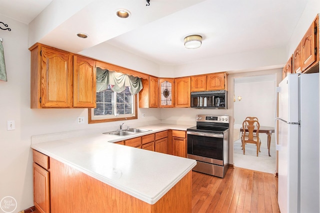 kitchen with stainless steel electric range oven, sink, kitchen peninsula, white fridge, and light wood-type flooring