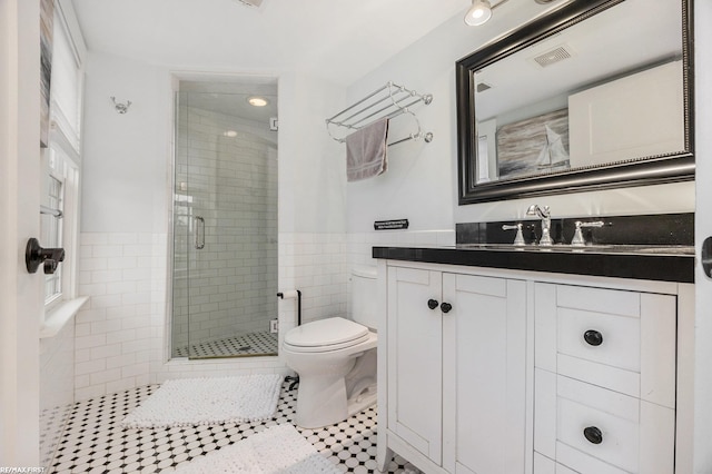 bathroom featuring tile patterned floors, toilet, vanity, a shower with shower door, and tile walls