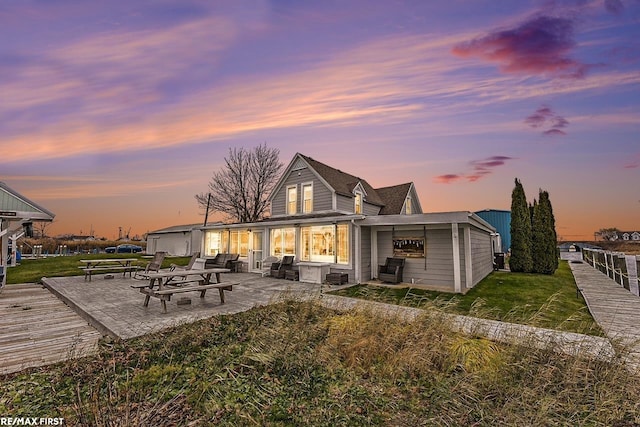 back house at dusk featuring a patio area and a yard