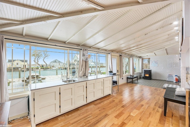 sunroom with a water view, a wood stove, lofted ceiling, and sink