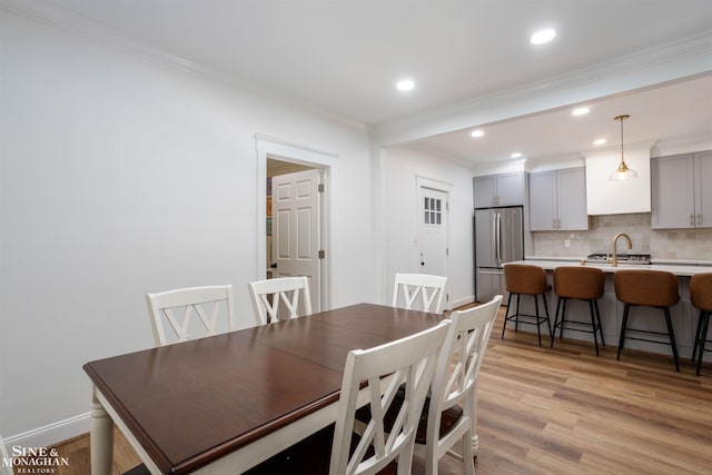 dining area featuring ornamental molding, sink, and light hardwood / wood-style flooring