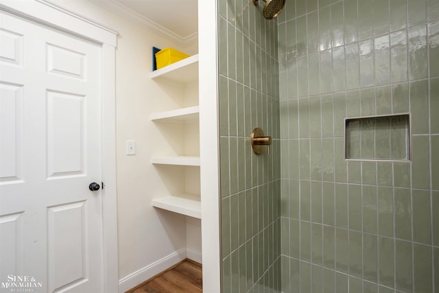 bathroom featuring a tile shower, built in shelves, crown molding, and wood-type flooring