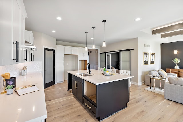 kitchen featuring sink, hanging light fixtures, light wood-type flooring, an island with sink, and white cabinetry