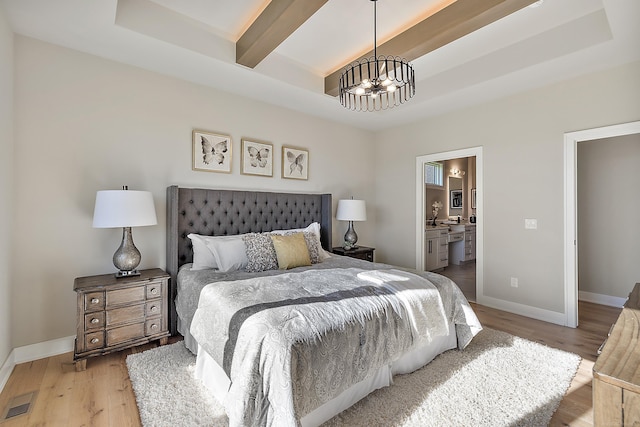 bedroom with a tray ceiling, ensuite bathroom, light hardwood / wood-style floors, and an inviting chandelier