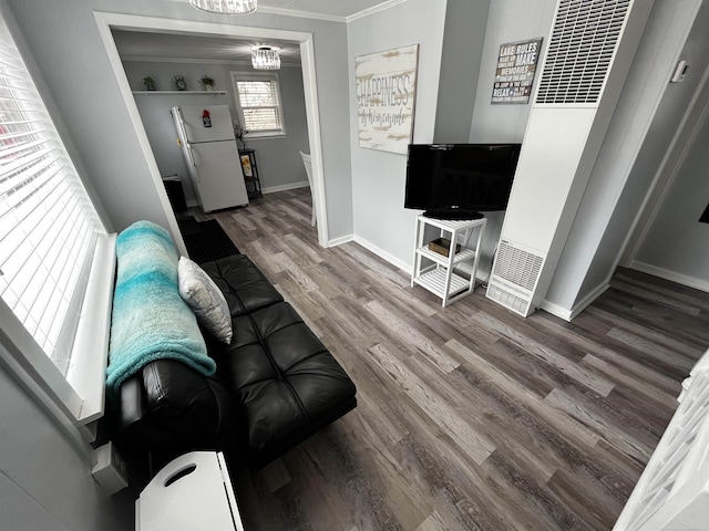 living room with wood finished floors, ornamental molding, baseboards, and a notable chandelier