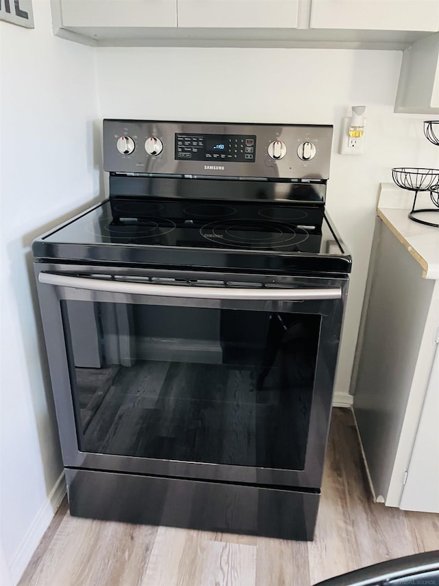 interior details with stainless steel electric range, white cabinetry, and light hardwood / wood-style flooring