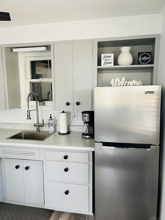 kitchen featuring white cabinetry, stainless steel refrigerator, ornamental molding, and sink