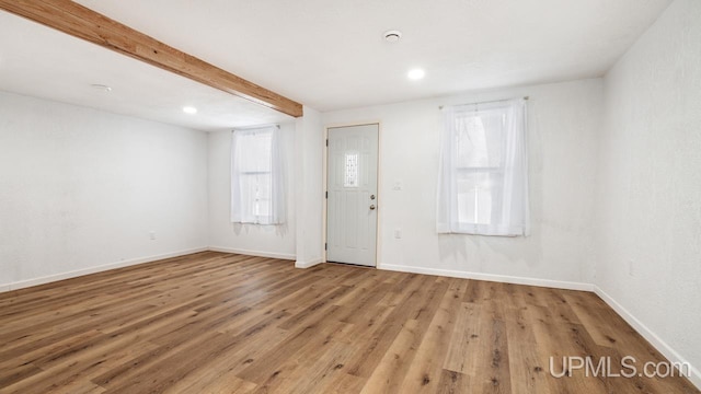 empty room with plenty of natural light, beamed ceiling, and light wood-type flooring