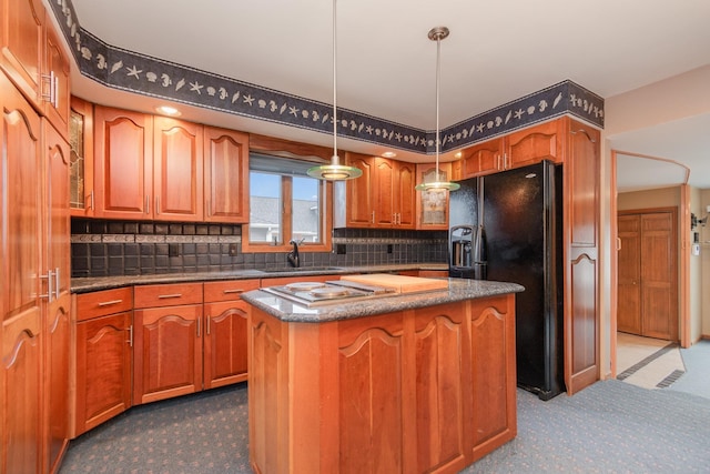 kitchen featuring hanging light fixtures, black fridge, decorative backsplash, a kitchen island, and sink