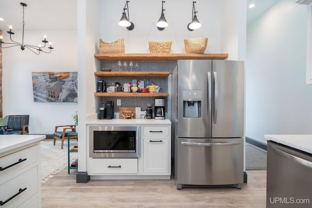 kitchen featuring white cabinetry, hanging light fixtures, a chandelier, appliances with stainless steel finishes, and light wood-type flooring