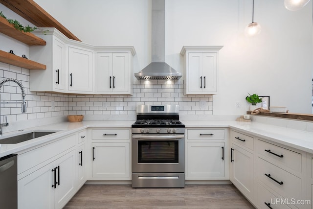 kitchen with appliances with stainless steel finishes, sink, wall chimney range hood, pendant lighting, and white cabinetry