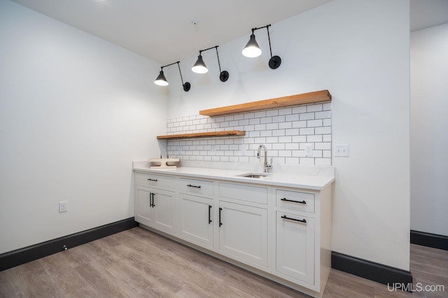 kitchen featuring decorative backsplash, light hardwood / wood-style floors, white cabinetry, and sink