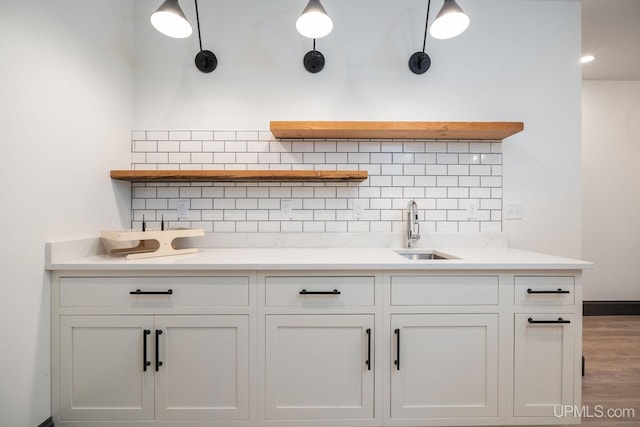 kitchen with hardwood / wood-style floors, white cabinets, sink, hanging light fixtures, and tasteful backsplash