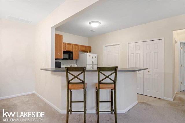 kitchen with white fridge, kitchen peninsula, light carpet, and a kitchen bar