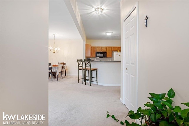 kitchen featuring white fridge, light brown cabinetry, a notable chandelier, light colored carpet, and a kitchen breakfast bar