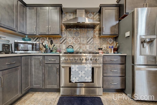 kitchen with light tile patterned flooring, decorative backsplash, dark brown cabinetry, wall chimney range hood, and appliances with stainless steel finishes