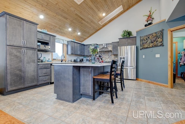 kitchen with a skylight, high vaulted ceiling, a kitchen island, stainless steel refrigerator with ice dispenser, and wall chimney range hood