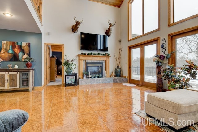 tiled living room with a towering ceiling, a tiled fireplace, and french doors