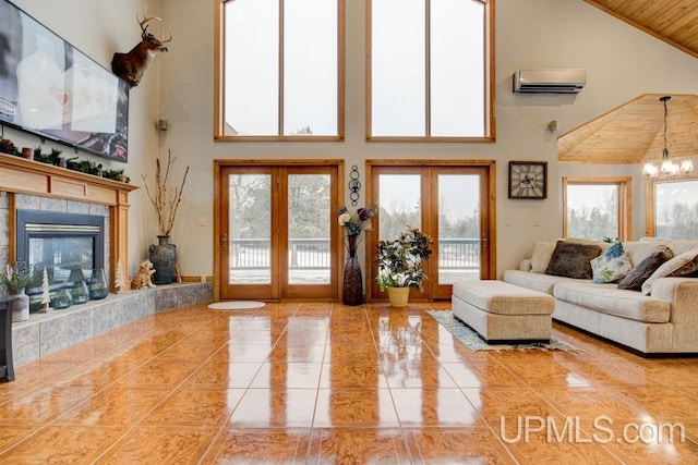 living room featuring a tile fireplace, a wall mounted AC, a towering ceiling, french doors, and an inviting chandelier