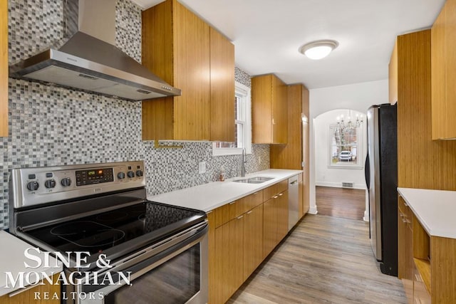 kitchen with sink, wall chimney exhaust hood, light hardwood / wood-style flooring, decorative backsplash, and appliances with stainless steel finishes