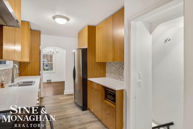 kitchen with stainless steel appliances, light wood-type flooring, a notable chandelier, sink, and tasteful backsplash