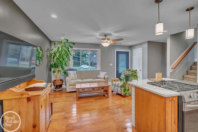 kitchen with stainless steel range with gas cooktop, light wood-type flooring, ceiling fan, and hanging light fixtures