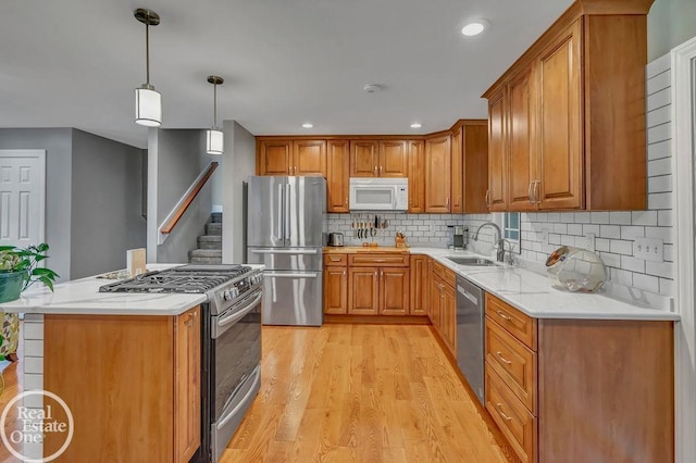 kitchen featuring appliances with stainless steel finishes, hanging light fixtures, sink, light hardwood / wood-style flooring, and backsplash