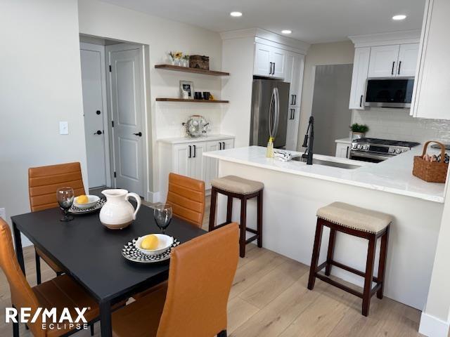 kitchen featuring sink, white cabinets, light hardwood / wood-style floors, decorative backsplash, and appliances with stainless steel finishes