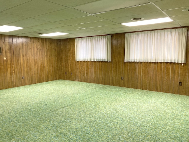 unfurnished room with carpet floors, a drop ceiling, and wood walls