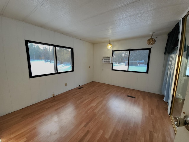 empty room with a wall mounted AC, a wealth of natural light, a textured ceiling, and hardwood / wood-style flooring