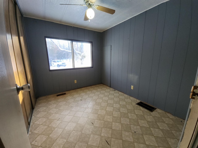 unfurnished room with ceiling fan and wooden walls