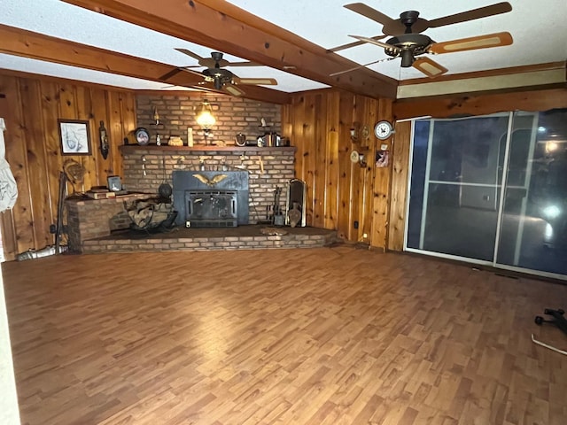 unfurnished living room featuring wood walls, beam ceiling, ceiling fan, and a wood stove