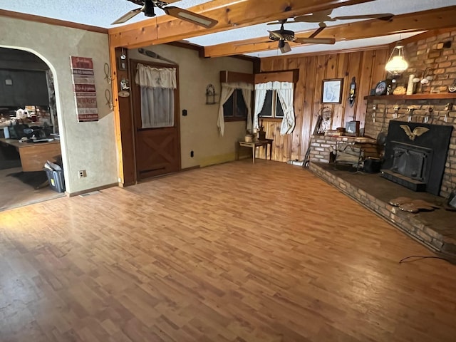 unfurnished living room featuring hardwood / wood-style flooring, a textured ceiling, a wood stove, beam ceiling, and ceiling fan