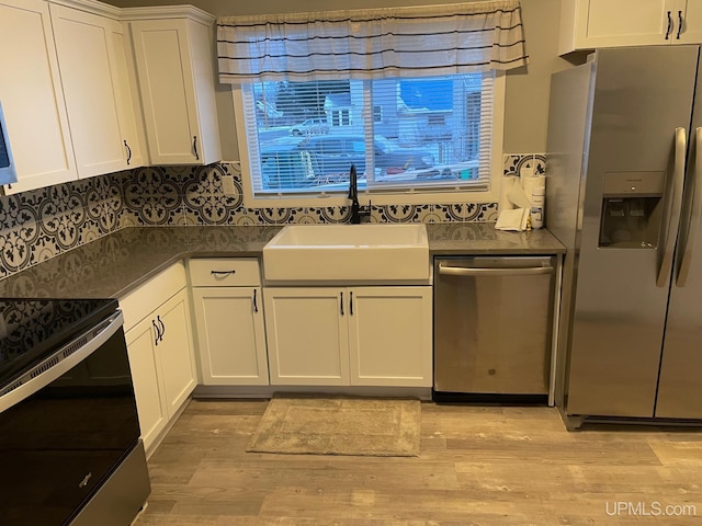 kitchen with appliances with stainless steel finishes, white cabinetry, light wood-type flooring, and sink