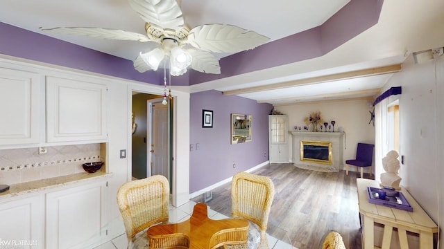 dining space featuring a premium fireplace, ceiling fan, light hardwood / wood-style floors, and beam ceiling