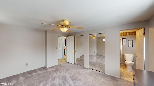 unfurnished bedroom featuring ensuite bath, two closets, ceiling fan, and light colored carpet