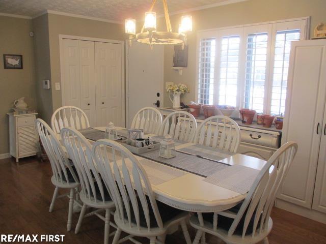 dining space featuring dark wood-type flooring, a notable chandelier, and crown molding